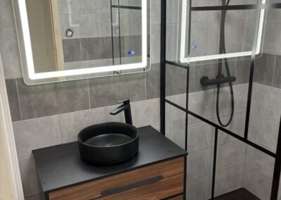 Photographie d'une rénovation de salle de bain moderne, noir, bois et pierre, avec un miroir lumière